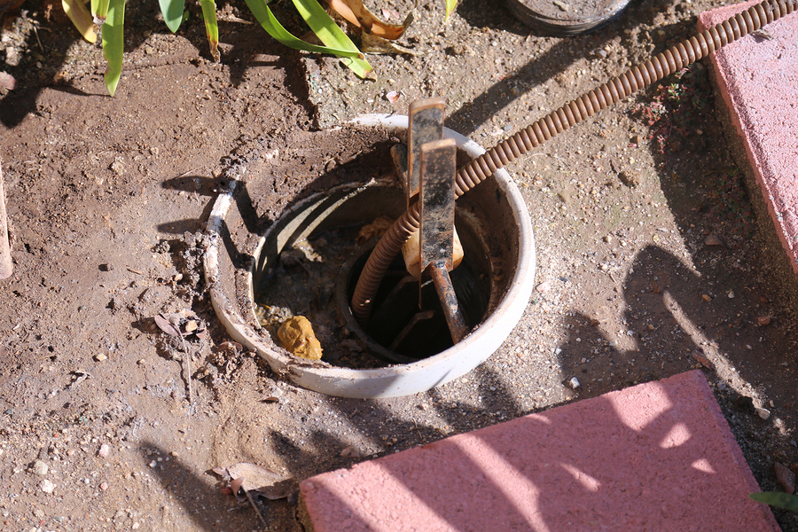 An Unidentifiable plumber unclogs a sewer drain with his Plumbing Snake and tools.